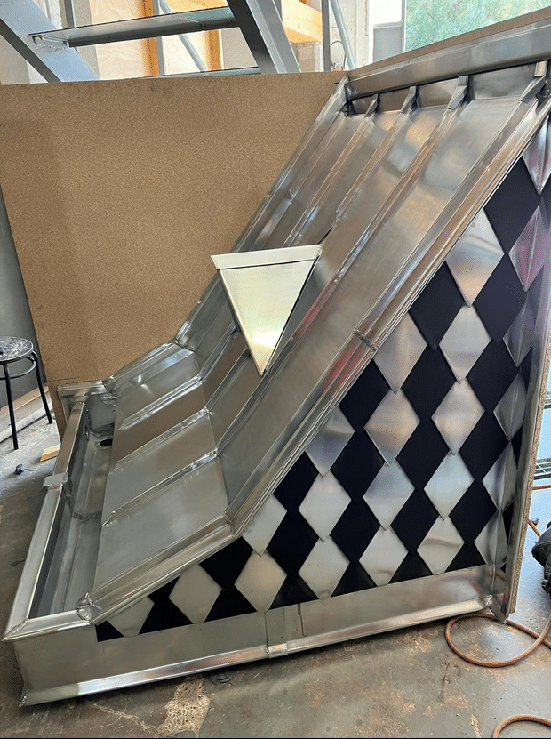 Hotet Métallique Personnalisée Tôle et Losanges Structure en tôle d'acier galvanisé et panneaux à motifs losanges noirs et argentés, peut-être une hotte ou un élément architectural en cours de fabrication.