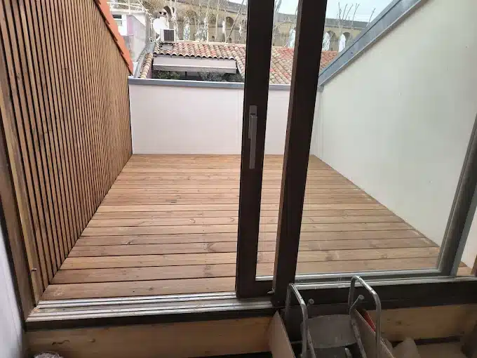 Terrasse en bois et revêtement mural moderne Terrasse en bois neuve vue depuis une baie vitrée coulissante, avec revêtement mural à lames verticales en bois.