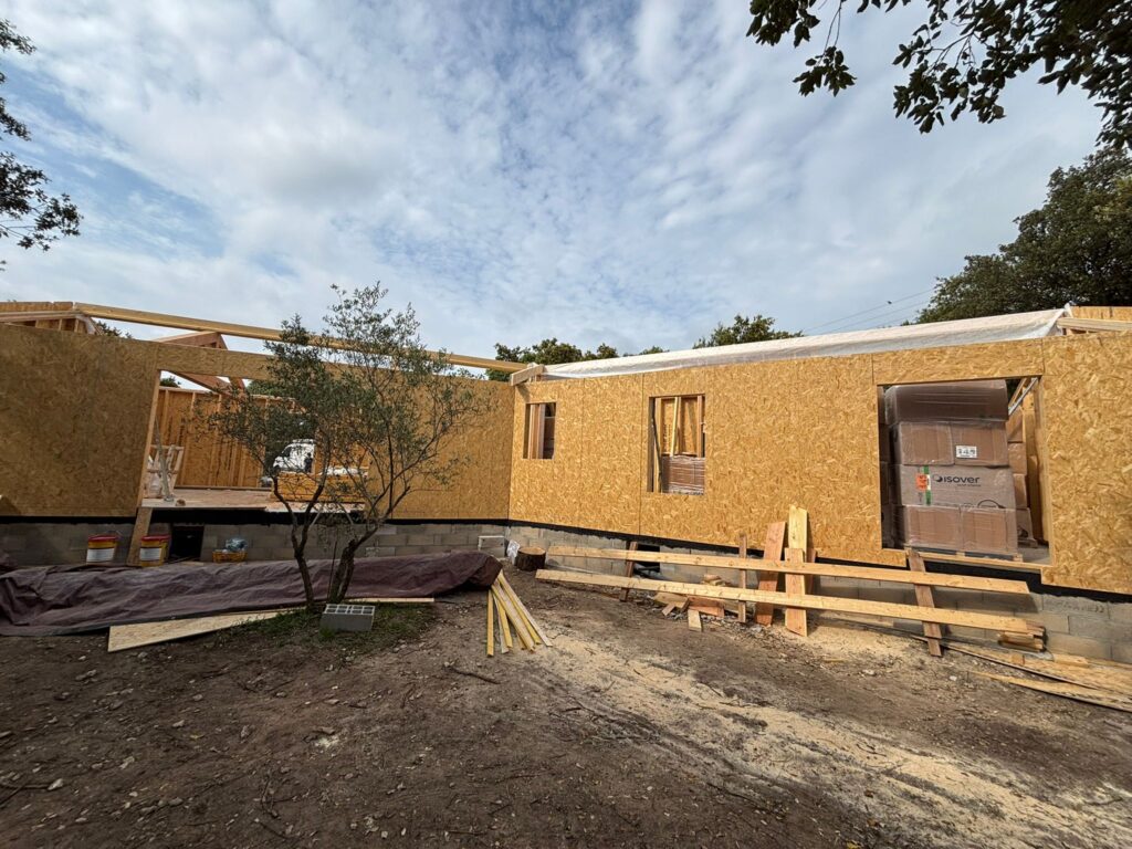 Chantier de maison à ossature bois avec panneaux OSB et isolant Isover sous un ciel nuageux.