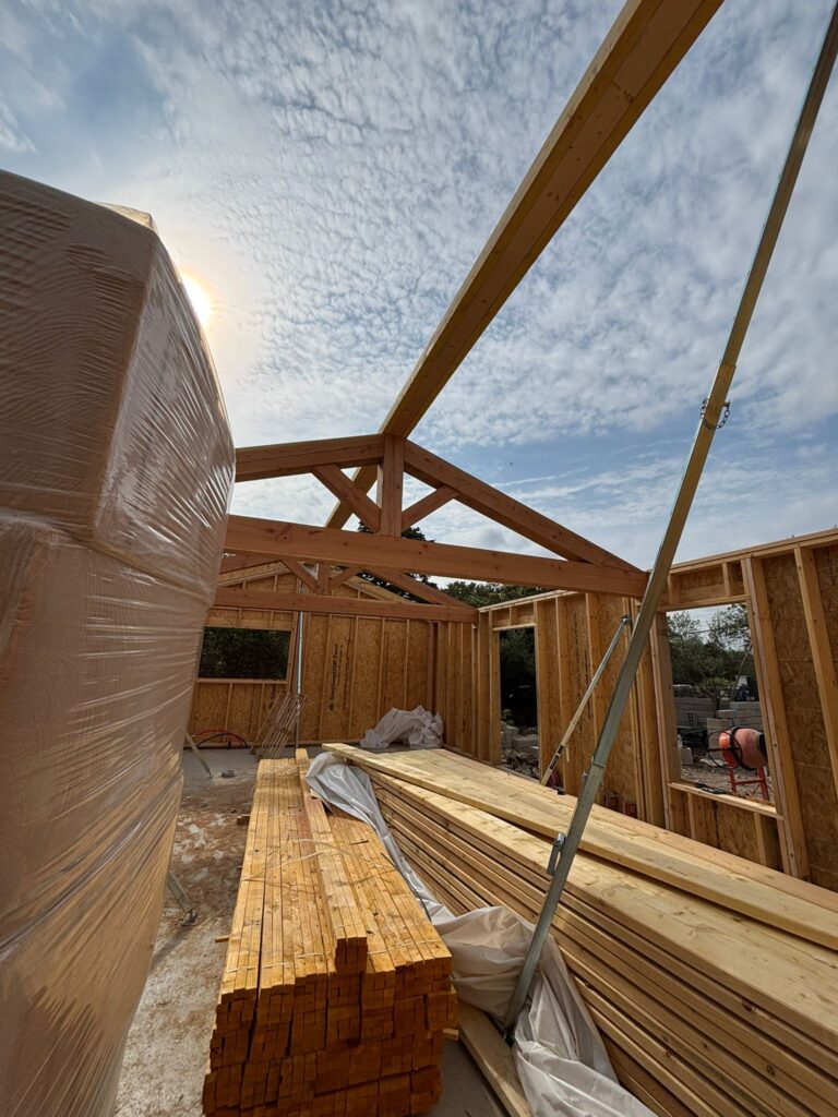 Charpente bois d'une maison individuelle en construction, piles de bois sur chantier sous un ciel ensoleillé.