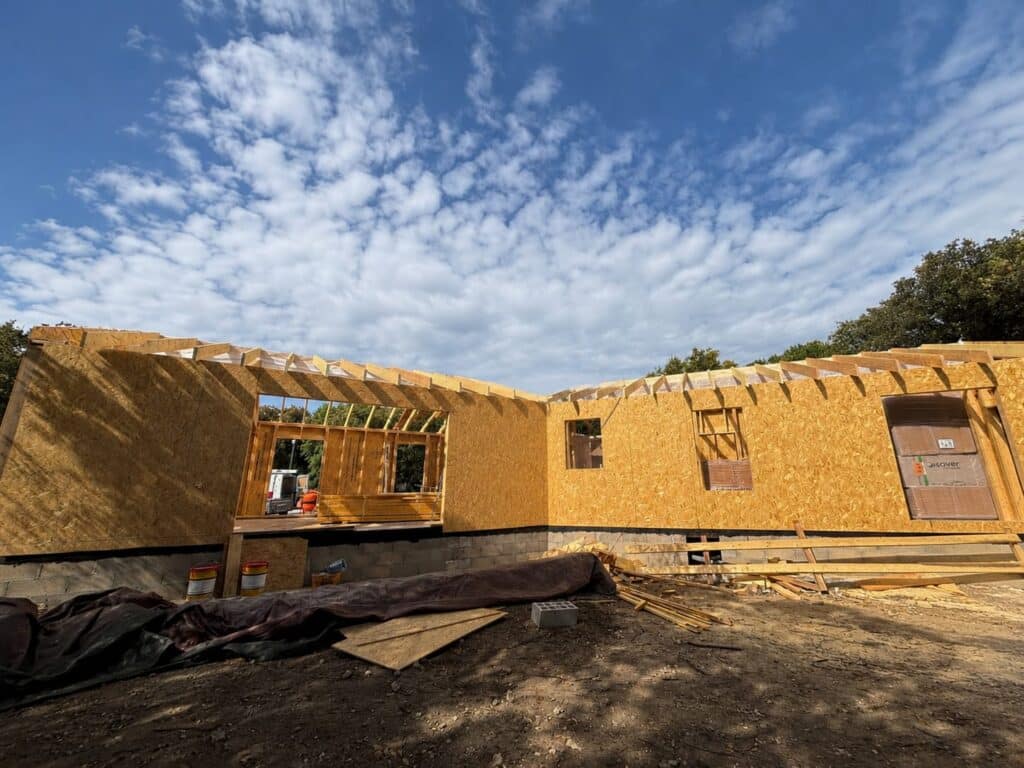 Maison en bois en construction avec panneaux OSB, charpente apparente et isolant Isover sous un ciel nuageux.