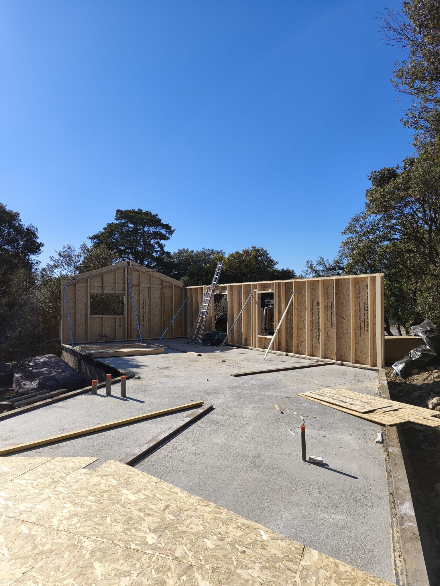 Rénovation Maison : Charpente Bois et Chantier Intérieur en cours de rénovation avec charpente en bois apparente, débris et planches sur un sol brut près d'une fenêtre baignée de lumière.