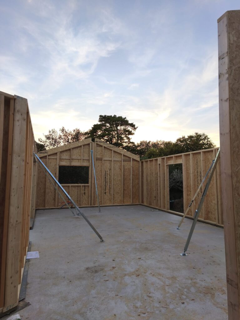 Ossature bois de maison sur dalle béton avec étais métalliques de soutien au coucher du soleil.
