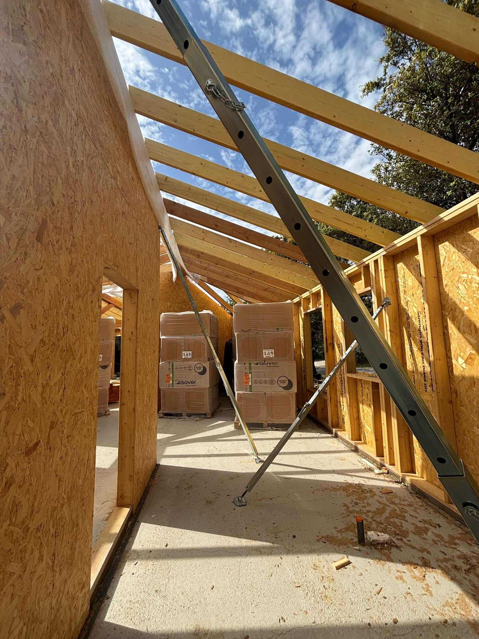 Rénovation Maison : Charpente Bois et Chantier Intérieur en cours de rénovation avec charpente en bois apparente, débris et planches sur un sol brut près d'une fenêtre baignée de lumière.