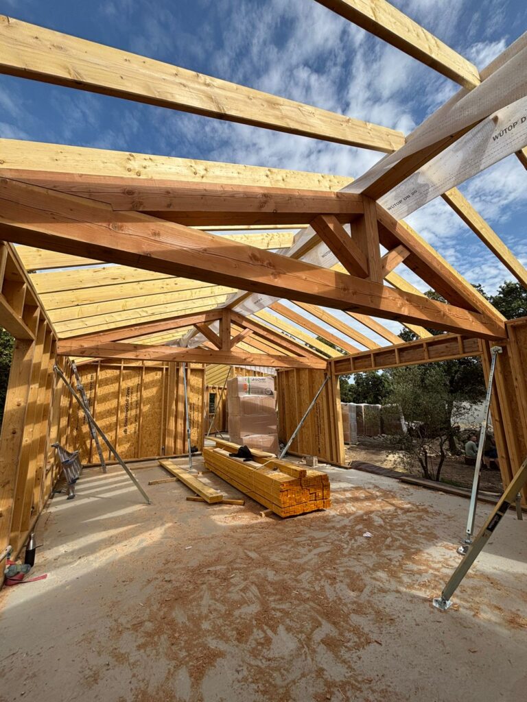 Structure bois de maison en construction avec charpente apparente, isolant ISOVER et pare-vapeur WÜTOP sous ciel bleu.